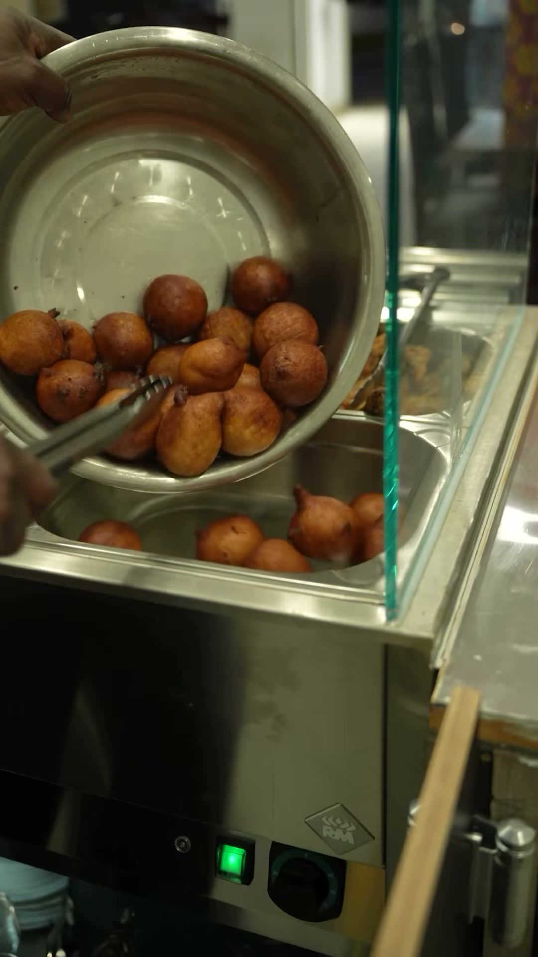 Frisch frittierte Bofrot werden aus einer Schüssel in die Warmhaltetheke gegeben