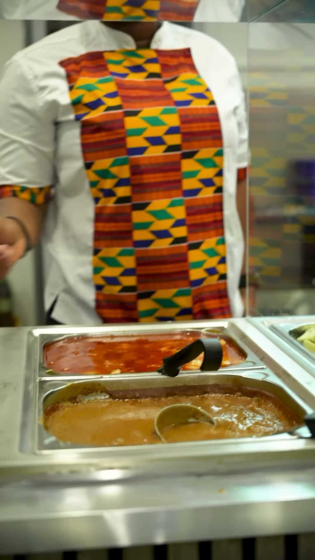 Person in Kente-Weste schöpft Soße am Buffet